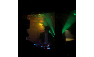 A DJ stands behind a mixing console in a dark room. Colorful beams of light create a vibrant atmosphere.