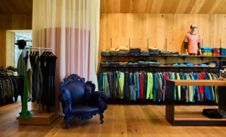 Ein modernes Geschäft mit einer Vielzahl von Kleidung in lebhaften Farben. In der Ecke steht ein eleganter blauer Sessel.