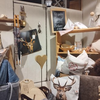 Ein gemütlicher Raum mit verschiedenen Kissen und Dekorationsartikeln. Auf einem Regal befinden sich Artikel mit Tiermotiven und Holzaccessoires. | © Abler Mittelberg | N. Lughammer