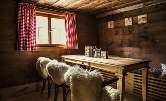 Ein gemütlicher Raum mit einem Holztisch und weichen Stühlen. Rote Fensterrahmen und Holzvertäfelung schaffen eine warme Atmosphäre. | © Kleinwalsertal Tourismus | Oliver Farys