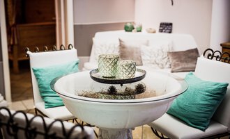 Ein stilvoller Innenraum mit einem gemütlichen Tisch und bequemen Stühlen. Auf dem Tisch stehen dekorative Gegenstände, die eine entspannte Atmosphäre schaffen. | © Verwöhn- & Wellnesshotel Walserhof| Aileen Melucci