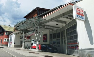 Eine moderne Tankstelle mit einer großen Überdachung steht an einer ruhigen Straße. Im Hintergrund sind Wohngebäude und ein bewölkter Himmel zu sehen. | © Kleinwalsertal Tourismus | N. Lughammer