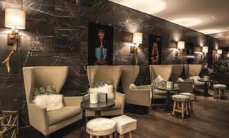 A modern café with cozy seating areas and stylish decor. The walls are decorated with artistic pictures, and there is soft lighting. | © A-ROSA Ifen Hotel Kleinwalsertal
