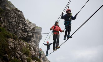 A group of climbers is pulling on a rope in the mountains.  
Everyone is wearing helmets and harnesses while they work on a rock face. | © Bergschule Walser Klettersteig @Bergschule Kleinwalsertal Oliver Farys