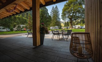 Eine gemütliche Terrasse mit einem Tisch und Stühlen, umgeben von Bäumen und Wiesen. Im Hintergrund sind Wohnmobile auf einem Campingplatz zu sehen. | © Campingplatz Vorderboden GmbH | Marion Schwendiger