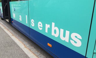 A bus with the inscription "walserbus" in an inviting turquoise color. The image shows the side of the bus, which is standing at a bus stop. | © Kleinwalsertal Tourismus