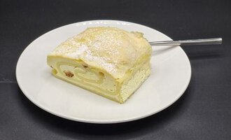 A piece of sponge roll on a white plate. The cake is dusted with powdered sugar and has a filling.