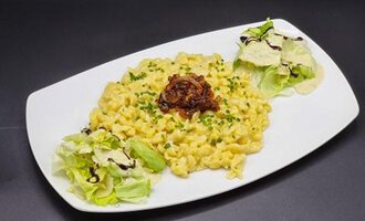 Ein Teller mit cremigen Makkaroni und Käse, garniert mit Röstzwiebeln. Daneben befinden sich frischer Salat und ein Dressing.