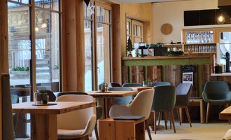 A modern café with wooden furniture and large windows. The colorful chairs and cozy atmosphere invite you to linger.