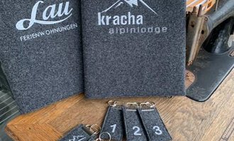 A wooden tray with keychains and two menus in a rustic setting. The tags are numbered and feature mountain motifs. | © Chrömle Schönes aus Filz | Anke Drechsel