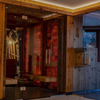 A modern reception area with wooden elements and large glass surfaces. The cozy atmosphere is enhanced by warm lighting and tasteful decorations. | © IFA Hotel Alpenhof Wildental | Andreas Froschauer