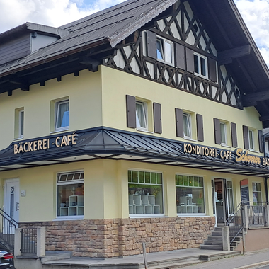 Ein hübsches Café mit einer Bäckerei in einem traditionellen Gebäude. Im Hintergrund sind Berge und ein blauer Himmel sichtbar. | © Kleinwalsertal Tourismus | Steffen Stöhr