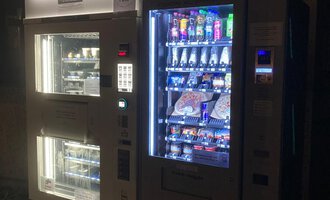 Ein Verkaufsautomat in der Dunkelheit mit einer Vielzahl von Snacks und Getränken. Der Automat leuchtet und bietet eine bunte Auswahl für die Kunden.