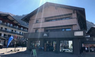A modern building with several floors that has a commercial facade. It is located in a picturesque alpine village setting. | © Sport Hilbrand GmbH