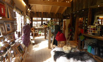 A cozy shop with wooden paneling and large windows. Pictures hang on the walls, and there are various crafts and decorations.