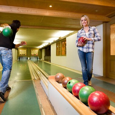 Eine gemütliche Kegelbahn mit zwei Personen, die spielen. Eine Person wirft eine Kugel, während die andere auf der Bahn steht und eine Kugel in der Hand hält. | © Aparthotel Kleinwalsertal Haller GmbH & Co KG