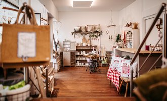 Ein einladendes Geschäft mit Holzfußboden und stilvollen Dekorationen. Regale sind gefüllt mit verschiedenen Produkten und gemütlichen Accessoires.