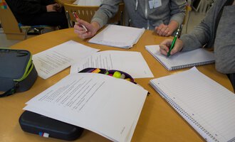 A group of people is working at a table with notes and writing materials. Various sheets and notebooks are on the table. | © Kleinwalsertal Tourismus