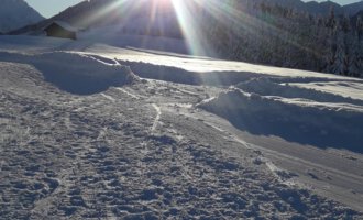 A sunny winter landscape with a snowy ground. The sun shines brightly behind the mountains, creating a bright, clear atmosphere. | © Panoramahütte