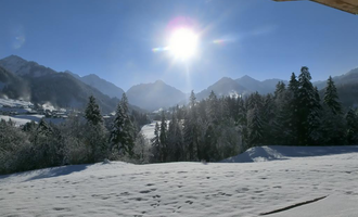A sunny winter landscape with snow-covered mountains and trees. The sky is clear blue and the sun shines brightly. | © Hotel Bellevue | I. Malouvier