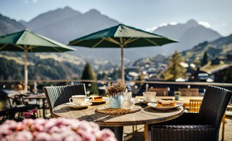 Ein schöner Tisch im Freien mit Blick auf die Berge. Auf dem Tisch stehen Kaffee, Gebäck und eine kleine Vase mit Lavendel.