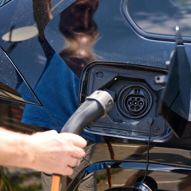 Eine Person lädt ein Elektroauto auf. Der Ladeanschluss ist geöffnet und eine Ladekabel wird eingesteckt. | © Kleinwalsertal Tourismus | Oliver Farys