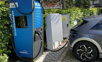 An electric charging station with an electric car that is currently being charged. The surroundings are green and peaceful, surrounded by trees. | © Energieversorgung Kleinwalsertal GmbH