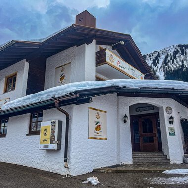A charming building in Alpine style, surrounded by snow and mountains. The facade is white and invites you to linger. | © Trattoria Pomo d'oro | K. Harmat-Hegedüs