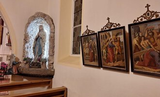 Eine Kirchengalerie mit einer Statue von Maria und mehreren historischen Gemälden an der Wand. Die Atmosphäre ist friedlich und andächtig. | © Unterwestegg-Kapelle Maria Hilf | Tanja Ritsch