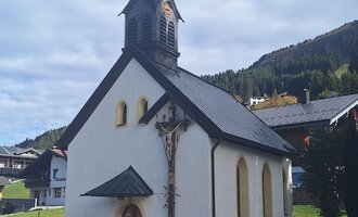 Eine kleine, weiße Kirche mit einem spitzen Turm und Holzelementen. Im Hintergrund sind grüne Hügel und Bäume sichtbar. | © Unterwestegg-Kapelle Maria Hilf | Tanja Ritsch