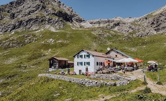 A picturesque mountain restaurant surrounded by green meadows and mountains. The clear sky provides a beautiful backdrop for the place. | © Widdersteinhütte  | Vanessa Wüstner