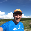 Ein lachender Mann in blauer T-Shirt und orange Mütze steht in einer grünen Landschaft bei schönem Himmel. | © Kleinwalsertal Tourismus eGen