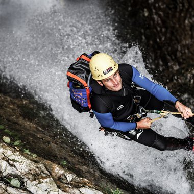 Abenteurer beim Klettern und Abseilen in einer Wasserfall-Umgebung, ausgesetzt an einem Seil, mit Helm und voller Ausrüstung. | © Kleinwalsertal Tourismus eGen • Fotograf: Dominik Berchtold