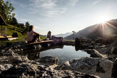 Woman sitting at the Naturerlebnisplatz Rohrweg, surrounded by rocks, overlooking mountains and sunset. | © Kleinwalsertal Tourismus eGen • Photographer: Dominik Berchtold