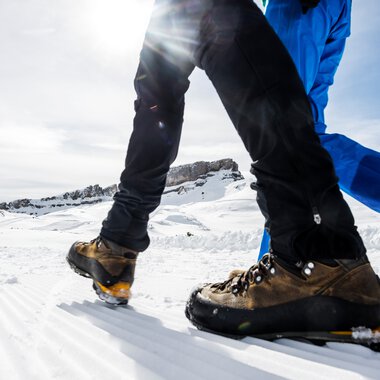 Nahaufnahme von zwei Personen beim Winterwandern mit Bergschuhen auf Schnee, Blick auf die Schuhe und das Bein im winterlichen Panorama. | © Kleinwalsertal Tourismus eGen • Fotograf: Dominik Berchtold