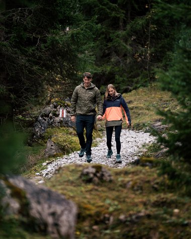 A couple walks hand in hand along a forest trail during daytime. | © Kleinwalsertal Tourismus eGen • Photographer: Hannah Bichay