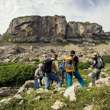 Gruppen von Wanderern unterwegs in einer bergigen Landschaft mit Felsen und grünen Wiesen. | © Kleinwalsertal Tourismus eGen • Fotograf: Oliver Farys