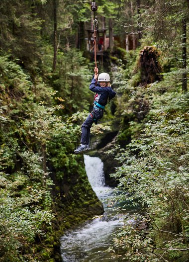Child ziplining over a stream in a lush green forest in Kleinwalsertal. | © Kleinwalsertal Tourismus eGen • Photographer: Oliver Farys