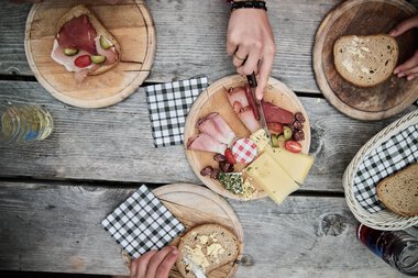 Breakfast table with bread, cheese, cold cuts, and drinks on a wooden surface during a hike in Kleinwalsertal. | © Kleinwalsertal Tourismus eGen • Photographer: Oliver Farys