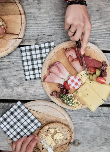 Breakfast table with bread, cheese, cold cuts, and drinks on a wooden surface during a hike in Kleinwalsertal. | © Kleinwalsertal Tourismus eGen • Photographer: Oliver Farys
