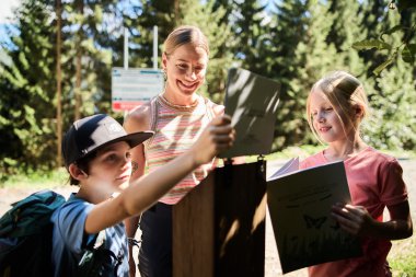 Drei Kinder und eine junge Frau beim Naturforscher-Abenteuer in den Bergen, alle lachen und schauen auf ein Tablet und einen Flyer. | © Kleinwalsertal Tourismus eGen • Fotograf: Oliver Farys