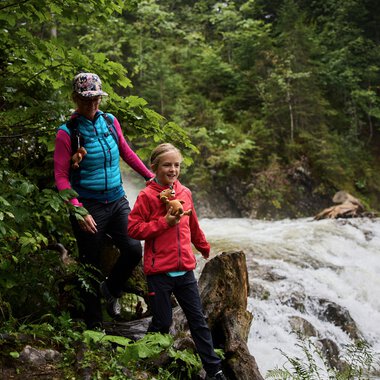 Zwei Personen beim Naturforscherabenteuer am Schwarzwasserbach im Kleinwalsertal, umgeben von grüner Natur, eine Person hält einen Frosch. | © Kleinwalsertal Tourismus eGen • Fotograf: Oliver Farys