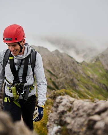 Exciting mountain climb with a smiling climber in gear and helmet in a rocky landscape. | © Kleinwalsertal Tourismus eGen • Photographer: Oliver Farys