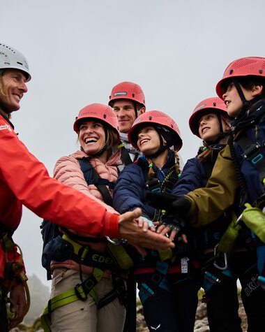 Gruppenfoto bei einem Klettersteig-Abenteuer in den Bergen, mit einer Bergführer-Person, die die Gruppe begrüßt oder willkommen heißt.