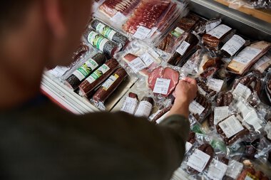 A person selects from a variety of vacuum-packed meat and sausages at a meat counter in Kleinwalsertal. | © Kleinwalsertal Tourismus eGen • Photographer: Oliver Farys
