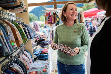 Frau verkauft handgefertigte Stoffe an einem Markt im Kleinwalsertal bei sommerlichem Wetter. | © Kleinwalsertal Tourismus eGen • Fotograf: Oliver Farys