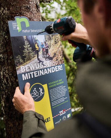 A ranger attaching an informational sign in the forest to promote nature conservation and education. | © Kleinwalsertal Tourismus eGen • Photographer: Oliver Farys