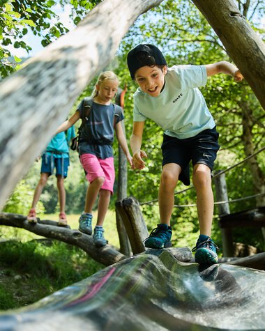 Children playing on a wooden bridge in the forest, laughing and exploring nature in Kleinwalsertal. | © Kleinwalsertal Tourismus eGen • Photographer: Oliver Farys