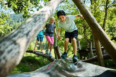 Kinder spielen auf einem Holzsteg im Wald, lachen und erkunden die Natur im Kleinwalsertal. | © Kleinwalsertal Tourismus eGen • Fotograf: Oliver Farys