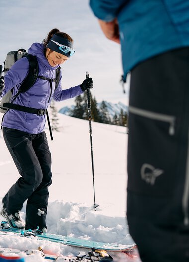 Frau beim Skitouren in verschneiter Berglandschaft, begleitet von einem Begleiter, mit Skiern und Touren-Ausrüstung. | © Kleinwalsertal Tourismus eGen • Fotograf: Oliver Farys